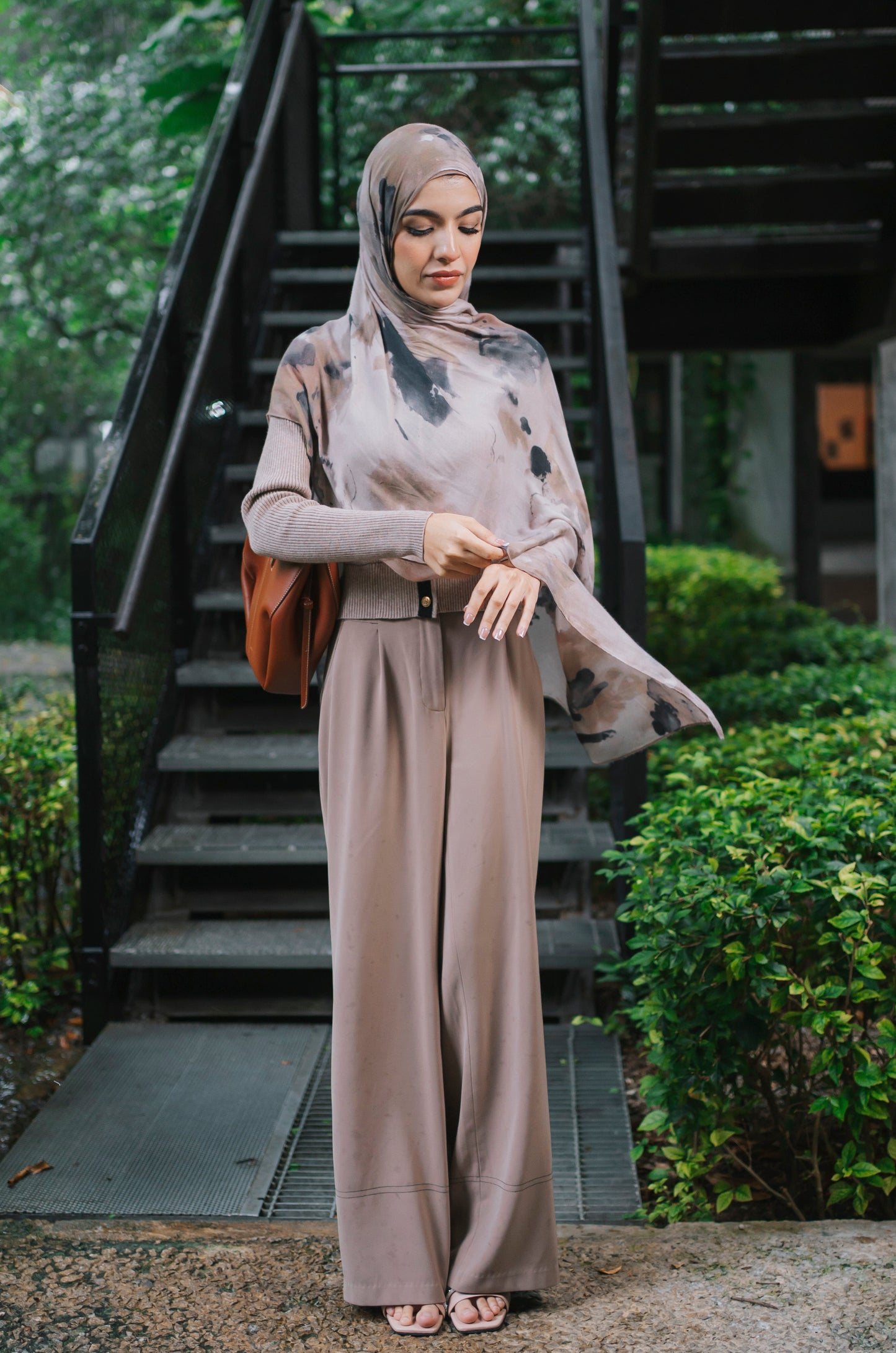 A woman wearing a taupe-beige two-tone modal hijab called stone-haze with a matching outfit. Stood in front of an outdoor staircase path.
